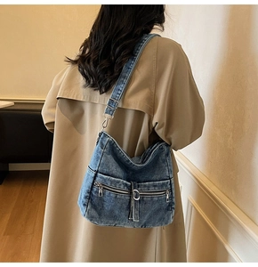 Detail of washed denim hobo bag with dual zipper pockets and adjustable metal strap buckle