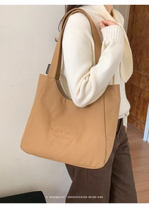 Detailed side view of khaki canvas tote bag featuring C'est la vie embroidery on shoulder