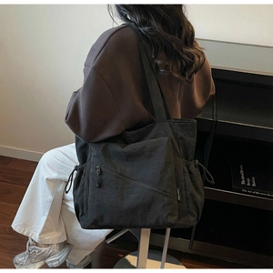 Detail of black nylon tote bag featuring functional diagonal zipper pocket and side drawstring