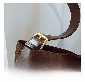 Detail shot of the golden metal buckle and adjustable suede strap on a brown shoulder bag