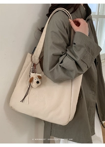 Detail of minimalist beige canvas tote bag with embroidery and cute puppy charm accessory