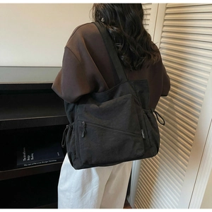 Detail of black tote bag featuring side drawstring, diagonal zipper and CK&BLLI woven label