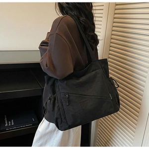 Detail of black nylon tote bag featuring side drawstring adjustment and front zipper pocket