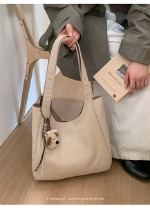 Detail of beige tote bag featuring C'est la vie embroidery and plush dog charm