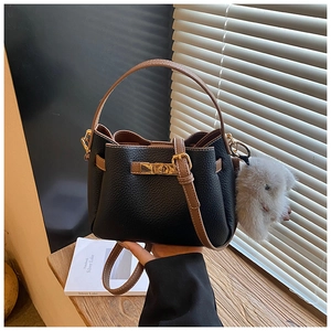 Detail of black pebbled leather bucket bag with brown handle and plush charm