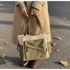 Outdoor close-up of a large canvas tote bag featuring olive green pockets and zippers