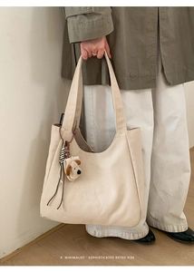 Detail view of cream canvas tote bag with embroidery, brand tag, and plush dog charm