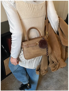 Detail of a brown woven texture bucket bag with a plush pom-pom charm and top handle
