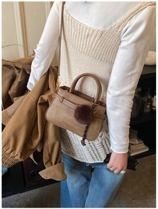 Detail of khaki woven crossbody bag with brown leather strap and decorative pompom charm