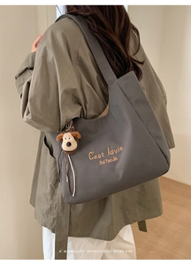Detail of grey canvas tote bag featuring C'est lavie embroidery and plush dog charm
