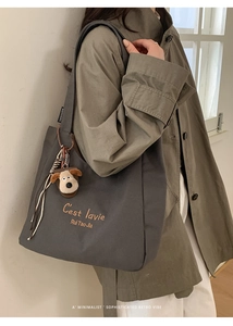 Close-up of gray canvas tote bag with brown embroidery and a cute dog plush charm