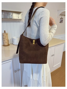 Detail of dark brown suede shoulder bag featuring a gold twist lock and textured finish