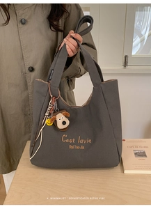 Detail of dark gray canvas tote bag with 'C'est la vie' embroidery and plush dog charm