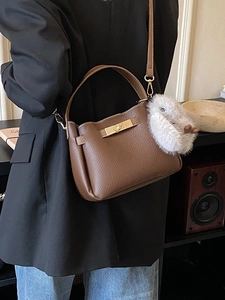 Brown lychee leather bucket bag with gold clasp and plush rabbit pendant decor