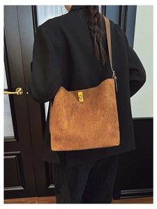 Detail view of brown suede bucket bag with gold metal buckle shown on a model's shoulder