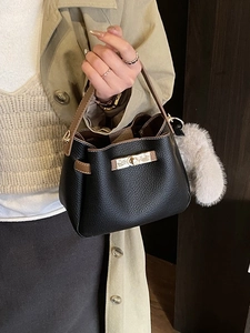 Elegant black bucket bag with brown handles and a plush charm on a beige trench coat