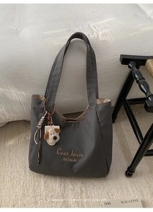 Detail of grey canvas tote bag featuring C'est la vie embroidery and plush puppy charm