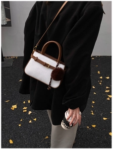 Detail of woven white bucket bag with brown leather handles and plush charm accessory