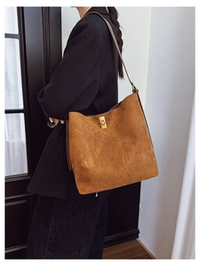 Detail of a brown suede tote bag featuring a gold metal lock and shoulder strap on a model