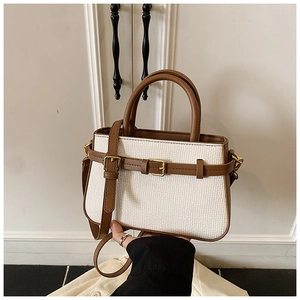 Detail of cream woven handbag with brown leather trim and golden metal buckle clasp
