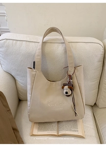 Detail view of beige canvas tote with C'est la vie embroidery and a cute puppy keychain