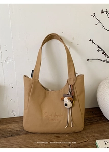 Detail of khaki canvas tote bag with embroidery, side label and a plush dog charm