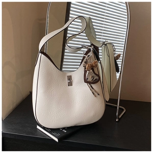 Detail of cream hobo bag with leather texture and heart mirror charm on a black table