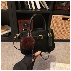 Détail d'un sac seau vintage en cuir noir avec boucle dorée et breloque pompon rouge