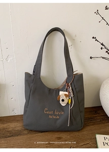 Detail of grey canvas tote bag with orange embroidery and plush dog charm on wooden desk