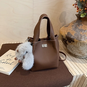 Detail of caramel brown litchi grain leather bucket bag with silver clasp and white fur charm