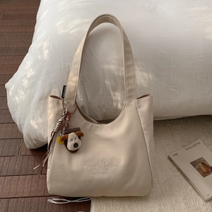Detail of beige canvas tote bag with letter embroidery and cute plush dog pendant