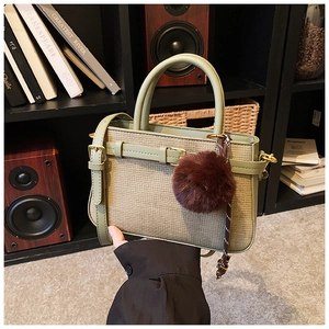 Detailed view of sage green woven texture handbag with plush ball and strap on shelf