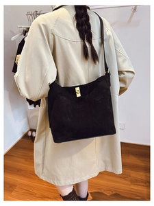 Close-up of black suede bucket bag with gold twist-lock buckle on a beige trench coat