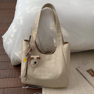 Detail of beige canvas tote bag with embroidery and a cute dog plush charm pendant