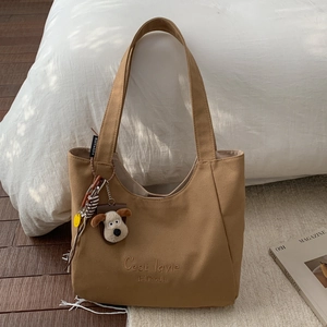Detail of khaki canvas tote bag with C'est la vie embroidery and plush puppy pendant