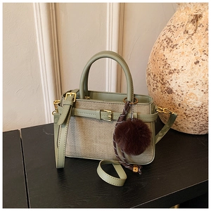Détail du sac seau vert sauge avec texture tissée, bandoulière cuir et pompon marron
