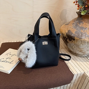 Detail of black lychee grain leather bucket bag with silver lock and plush rabbit charm