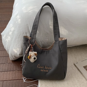 Detail of dark grey canvas tote with C'est la vie embroidery and cute dog plush charm