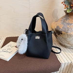Detail of black pebbled leather bucket bag with silver twist lock and plush rabbit charm