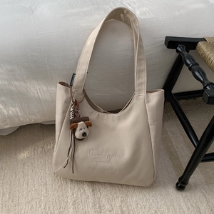 Close-up of cream canvas tote bag with C'est la vie embroidery and dog charm detail