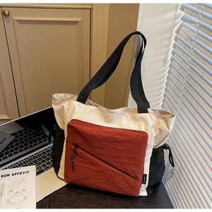 Detail view of a color-block tote bag with side drawstrings and diagonal zipper pocket