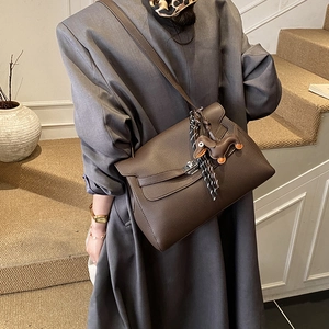 Detail of brown litchi leather tote with dog charm and geometric scarf on model
