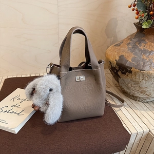 Detail of grey pebbled leather bucket bag featuring metal twist lock and plush bunny charm