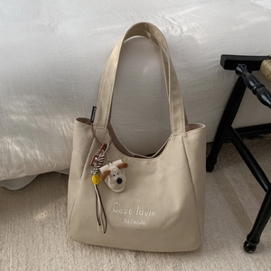 Close-up of beige canvas tote bag featuring C'est lavie embroidery and cute plush pendant