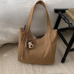 Detail of khaki canvas tote bag with 'C'est la vie' embroidery and plush dog charm accessory