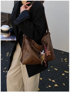 Brown leather tote bag with contrast stitching and plush charm in an autumn street setting