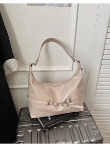 Detail of beige hobo bag with glossy finish and metal belt buckle on a silver suitcase