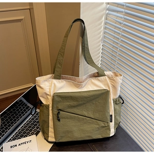 Detail of green and beige nylon tote bag featuring front zipper and side drawstring pocket