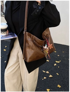 Detail of brown faux leather shoulder bag with white contrast stitching and bear charm