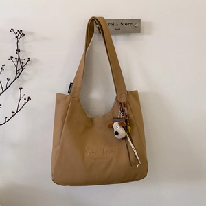 Close-up of khaki canvas tote bag featuring C'est la vie embroidery and dog plush charm